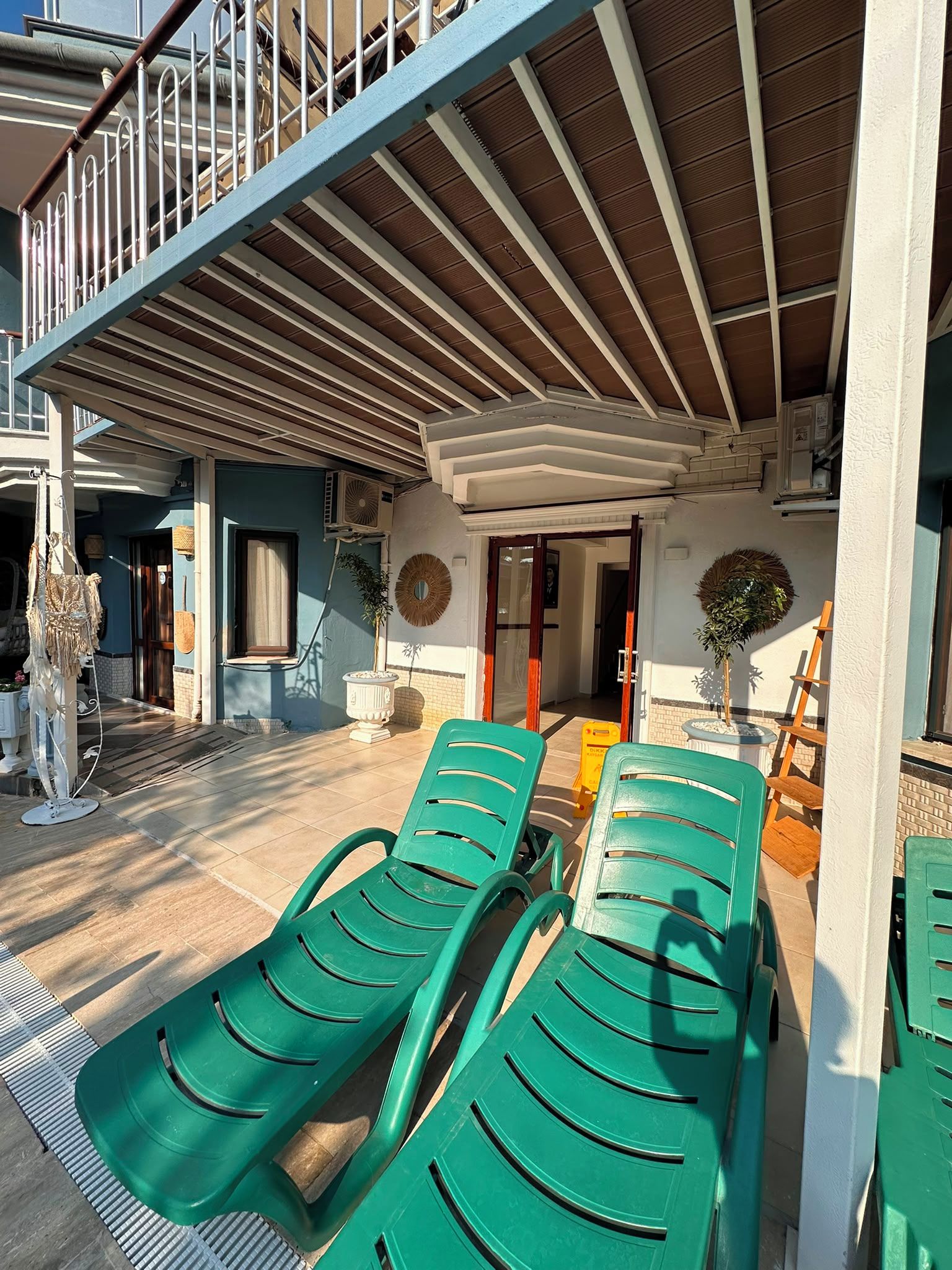 Ein überdachter Außenbereich mit grünen Lounge-Stühlen, einer Treppe und einem Hauseingang.