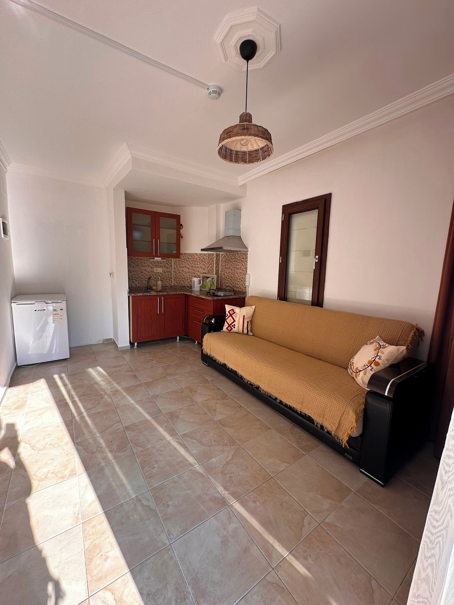A living room with a sofa, a kitchen area with cabinets, and a refrigerator.