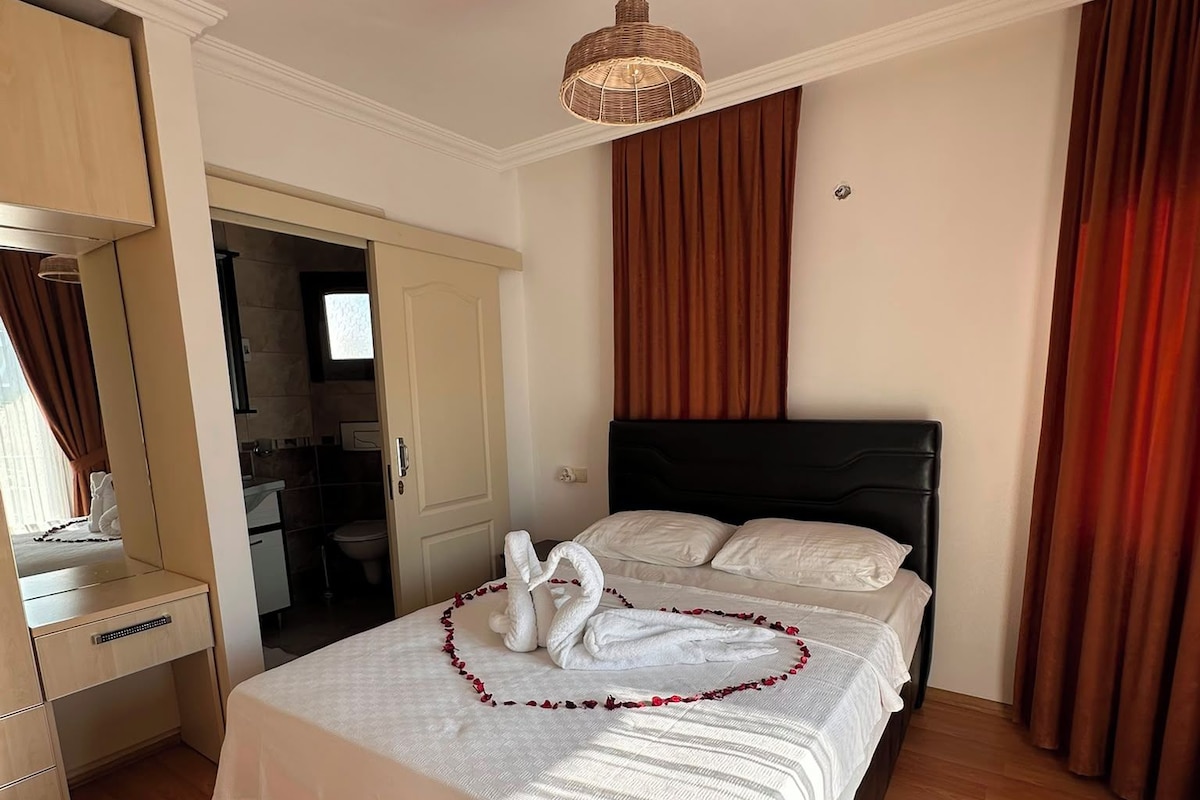 Quarto de hotel com uma cama grande, piso de madeira, espelho e luminária pendente.