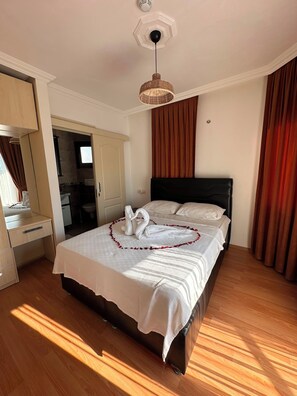 Quarto de hotel com uma cama grande, piso de madeira, espelho e luminária pendente.