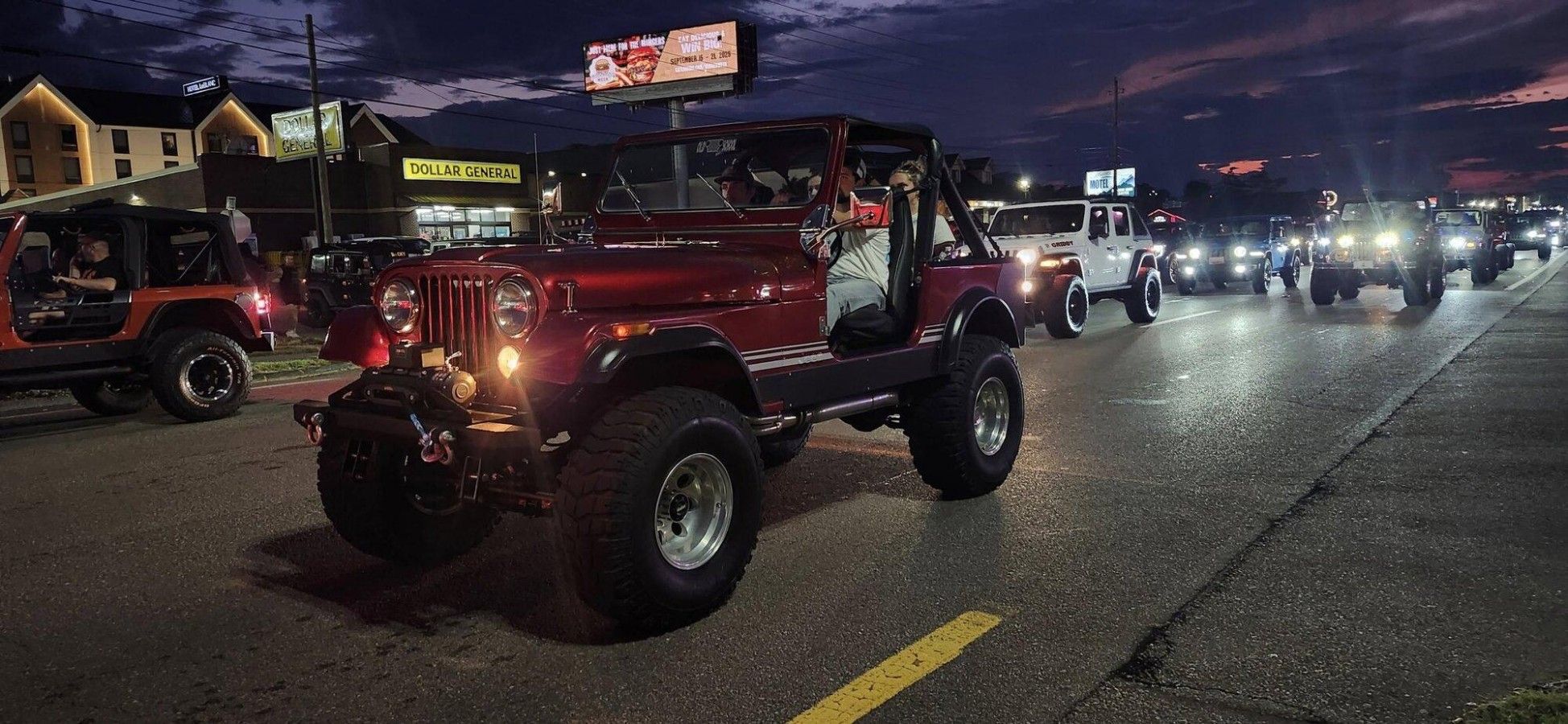 A red off-road vehicle on a wet road at night with other vehicles in the background.