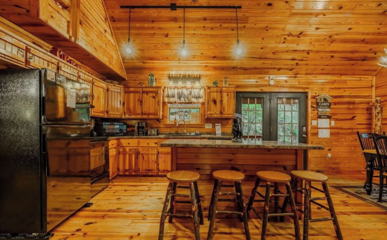 A cabin interior with a kitchen, bar stools, and a dining area.