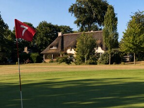 A golf course with a flag marked '7' in the foreground, a thatched-roof building in the background, and surrounding greenery. - Ravissant Cottage 7 Chambres au cœur de la Bretagne Romantique - 300 m² (Epiniac)