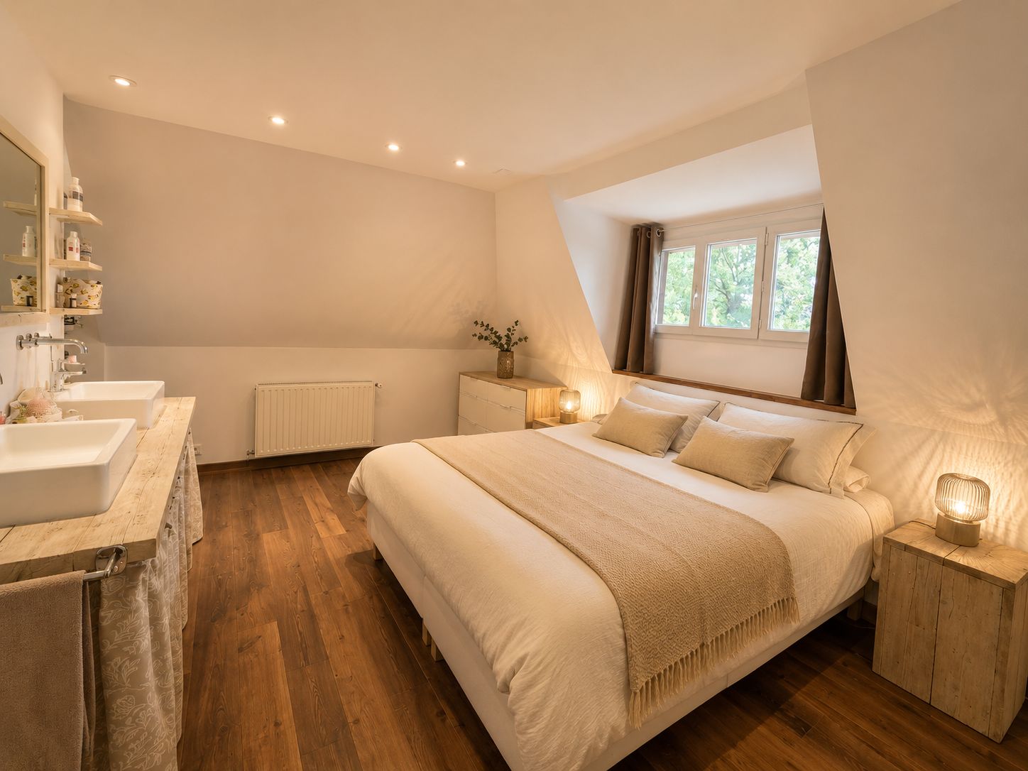 A bedroom with a large bed, bedside tables, a window with curtains, and a bathroom with a sink and mirror.