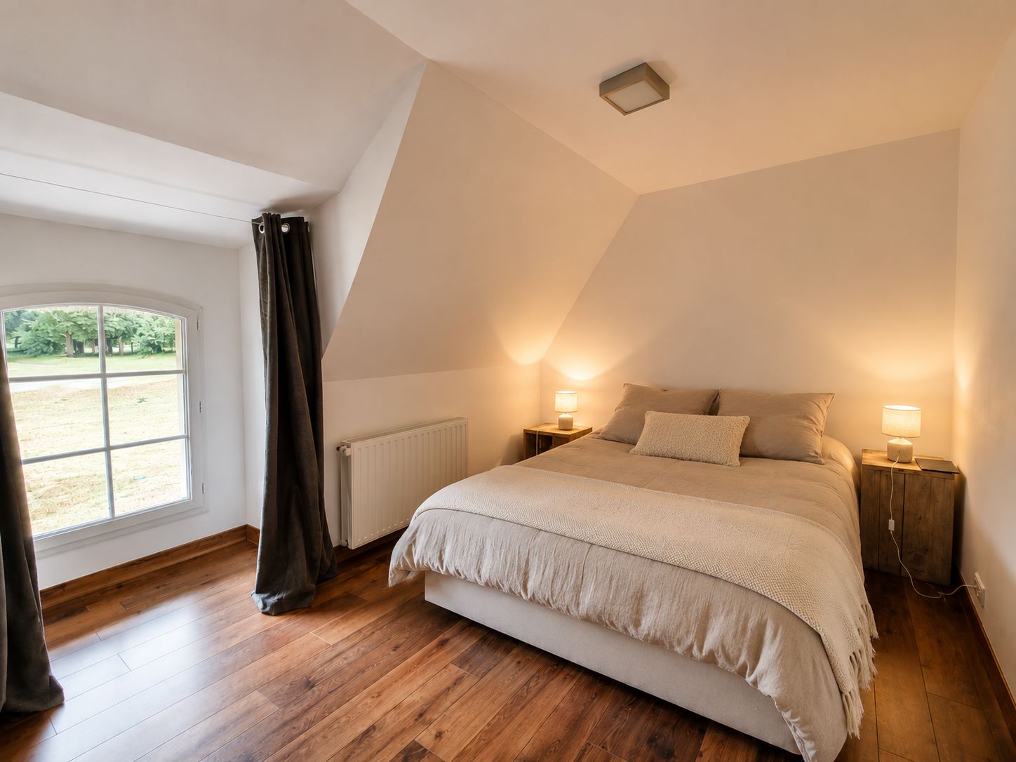 A bedroom with a sloped ceiling, a large window, and a bed with two bedside tables.