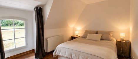 A bedroom with a sloped ceiling, a large window, and a bed with two bedside tables.