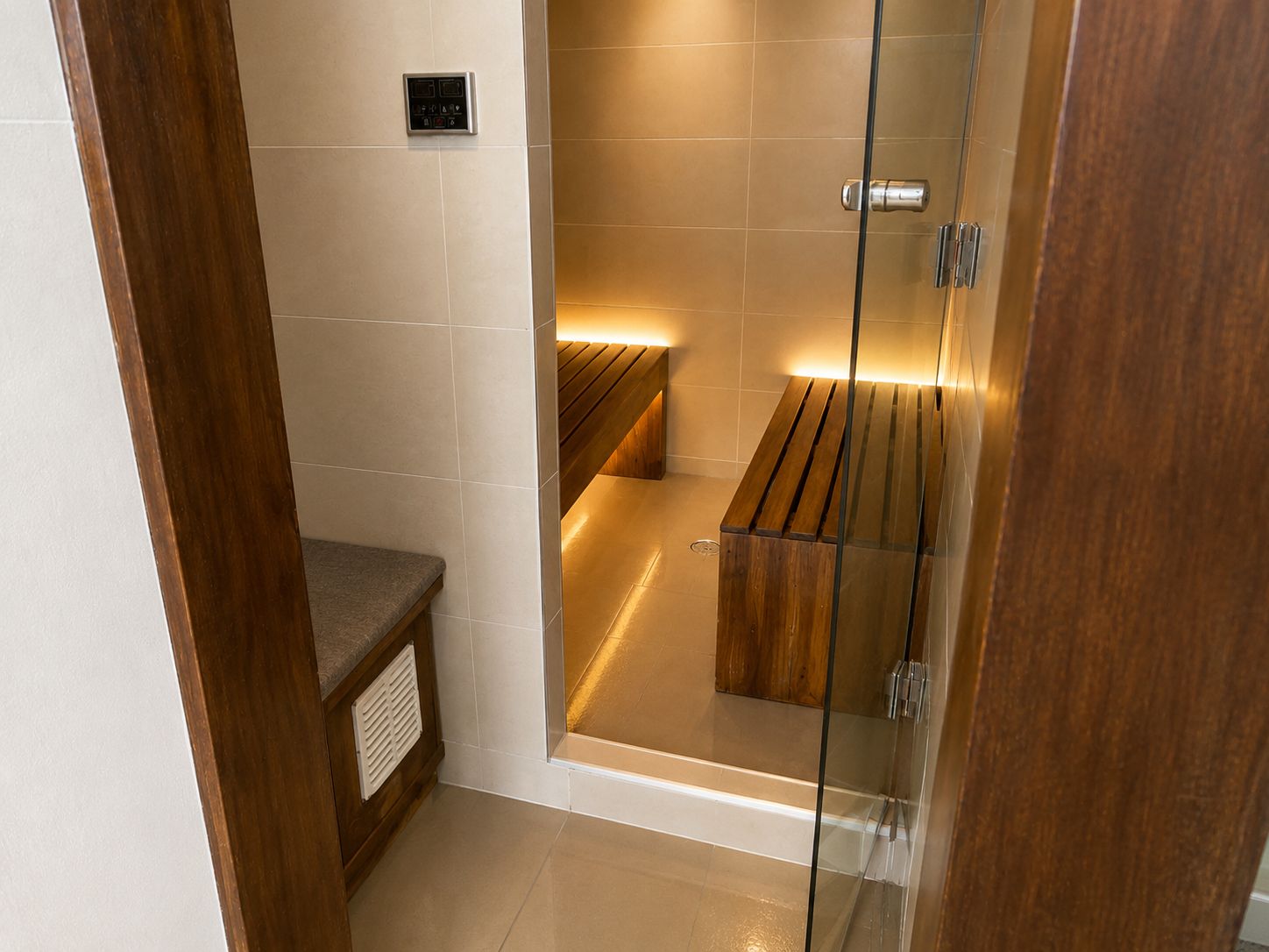 A modern bathroom with a glass shower enclosure, a wooden bench, and a control panel on the wall.