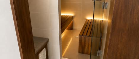 Un baño moderno con cabina de ducha de vidrio, un banco de madera y un panel de control en la pared.