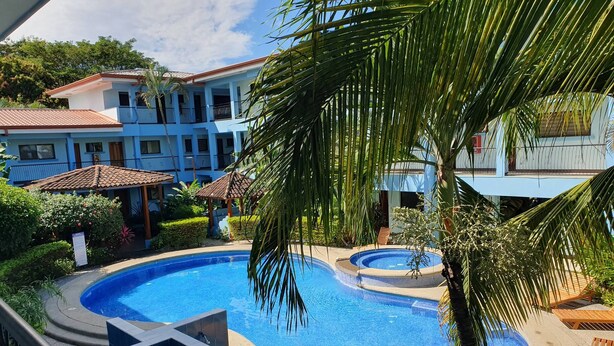 A swimming pool with a surrounding deck, palm trees, and a building with balconies in the background. - Marina Loft Studio # 218 (Sardinal)