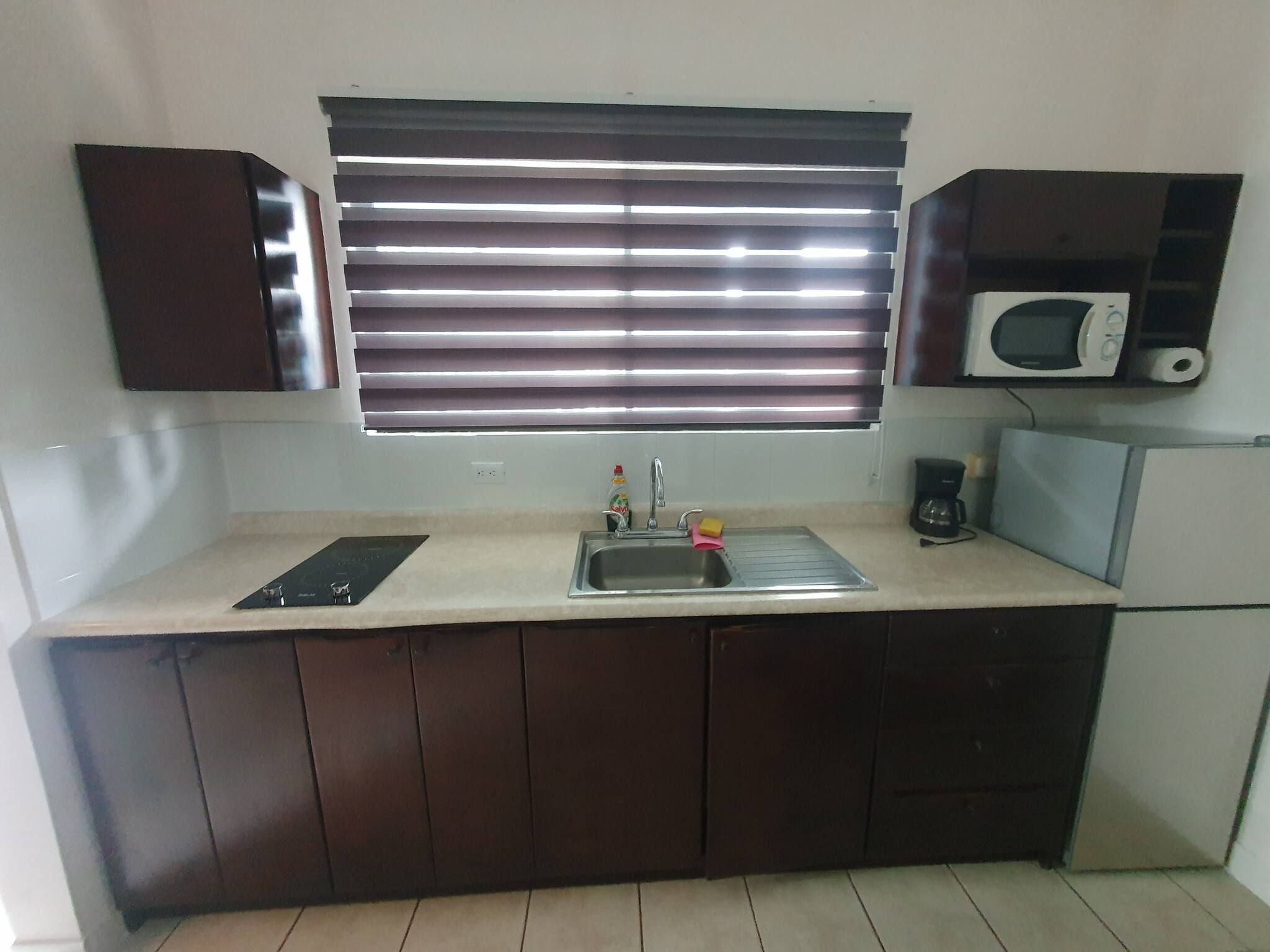 A kitchen with a built-in microwave, a sink, and a window with blinds.