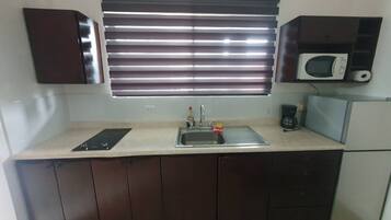 A kitchen with a built-in microwave, a sink, and a window with blinds.