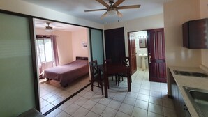 A room with a bed, a dining table with chairs, a ceiling fan, a sink, and a television. - Marina Loft Studio # 218 (Sardinal)