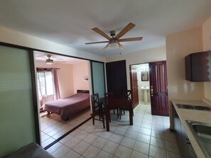 A room with a bed, a dining table with chairs, a ceiling fan, a sink, and a television. - Marina Loft Studio # 218 (Sardinal)