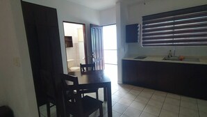 A living room with a dining table and chairs, a ceiling fan, and a kitchen area with a window. - Marina Loft Studio # 218 (Sardinal)