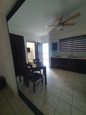 A living room with a dining table and chairs, a ceiling fan, and a kitchen area with a window. - Marina Loft Studio # 218 (Sardinal)