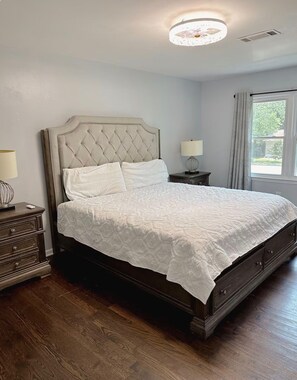 Un dormitorio con una cama grande, una mesita de noche, una lámpara y una ventana con cortinas.