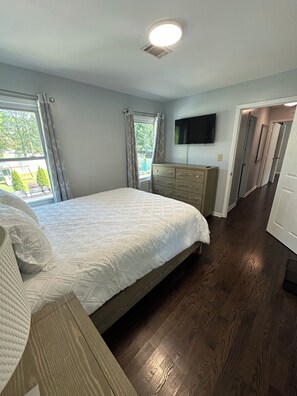 Un dormitorio con cama, cómoda, televisor y vistas al exterior.