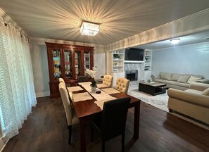 Un comedor con mesa y sillas de madera, un aparador con puertas de cristal, y un televisor en la sala de estar.