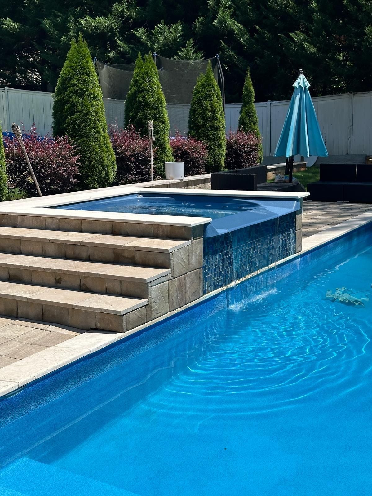 Piscina rectangular con hidromasaje integrado, rodeada de escalones de piedra y una valla.