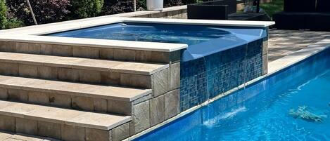 Piscina rectangular con hidromasaje integrado, rodeada de escalones de piedra y una valla.
