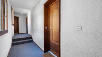 Un couloir avec une porte en bois, un sol recouvert de moquette et un petit tapis à l’entrée.