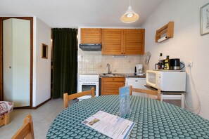Een kleine keuken met houten kastjes, een fornuis, een magnetron en een eettafel met een placemat.