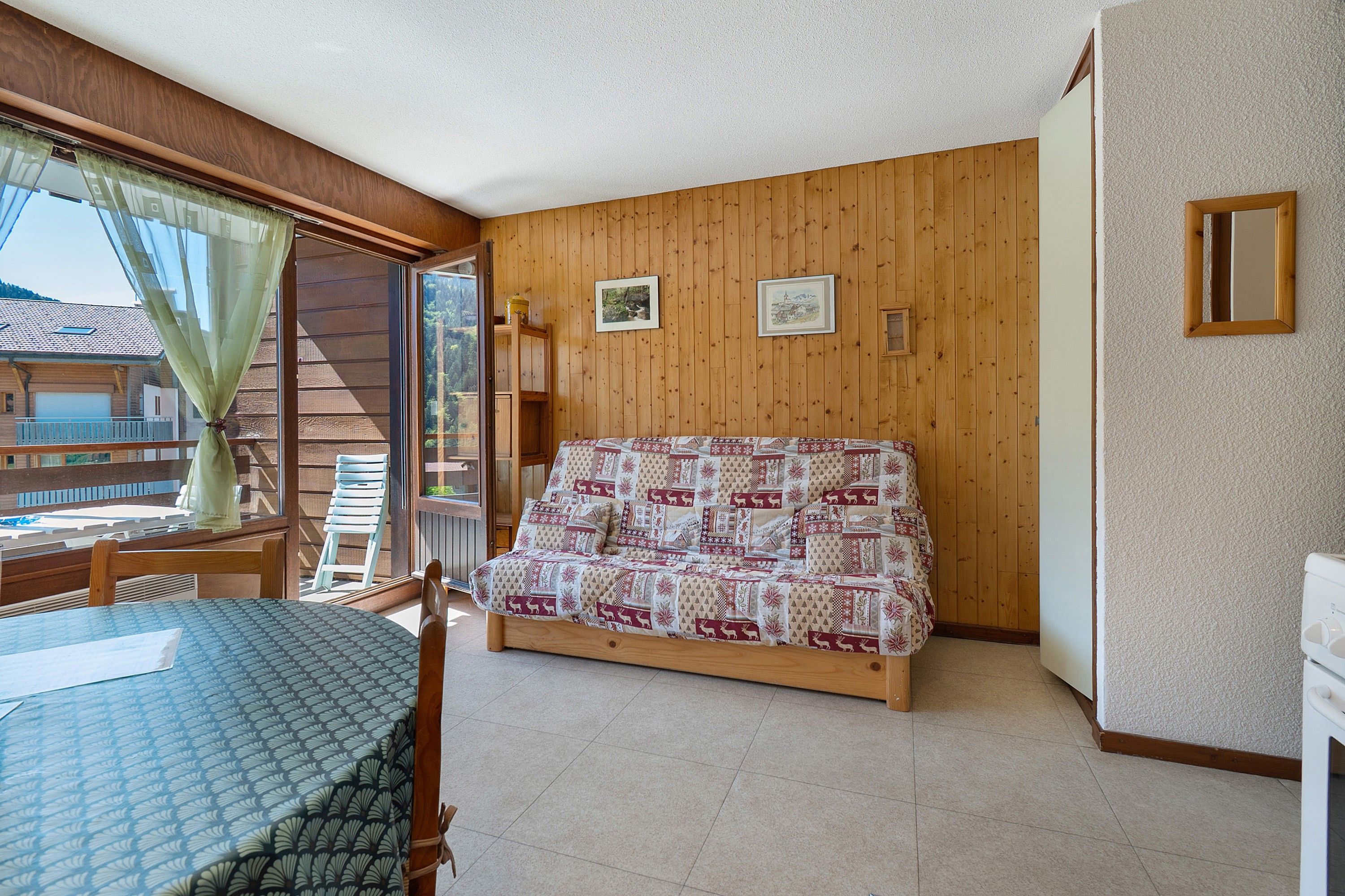 Une pièce comprenant un lit, une table et une chaise. Il y a une fenêtre avec des rideaux, un mur en bois et un cadre de tableau.