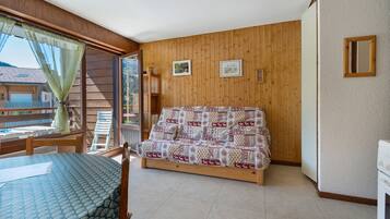 Une pièce comprenant un lit, une table et une chaise. Il y a une fenêtre avec des rideaux, un mur en bois et un cadre de tableau.
