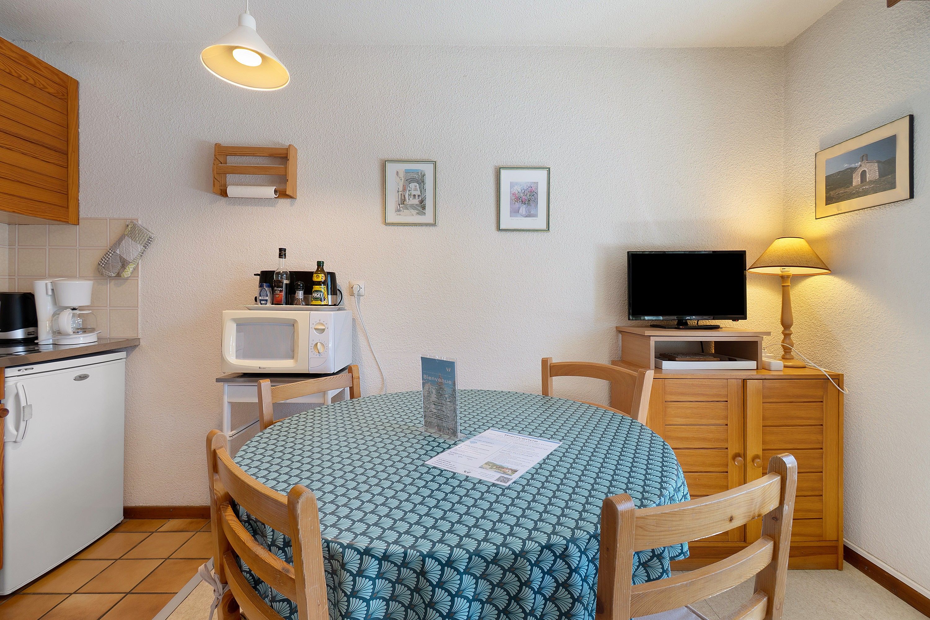 Une cuisine compacte comprenant une table à manger, des chaises, un four à micro-ondes, un petit réfrigérateur et un téléviseur.
