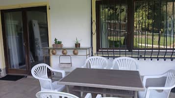 An outdoor patio with a table and chairs, a potted plant, and a window with a metal grill.