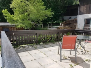 A patio with a wooden fence, a metal table with a glass top, and a red chair.