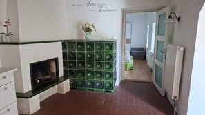 Eine Küche mit einer dunkelgrünen gefliesten Spritzschutzwand, einer weißen Wand mit einem deutschen Schriftzug, einer kleinen Vase mit Blumen und Blick in einen Wohnbereich.