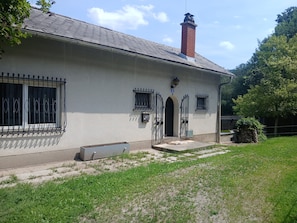 Ein eingeschossiges Gebäude mit Schornstein aus Ziegeln, einer kleinen Veranda und einem Metallgitter.