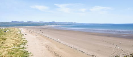 A coastal landscape with a sandy beach, a clear sky, and distant mountains.