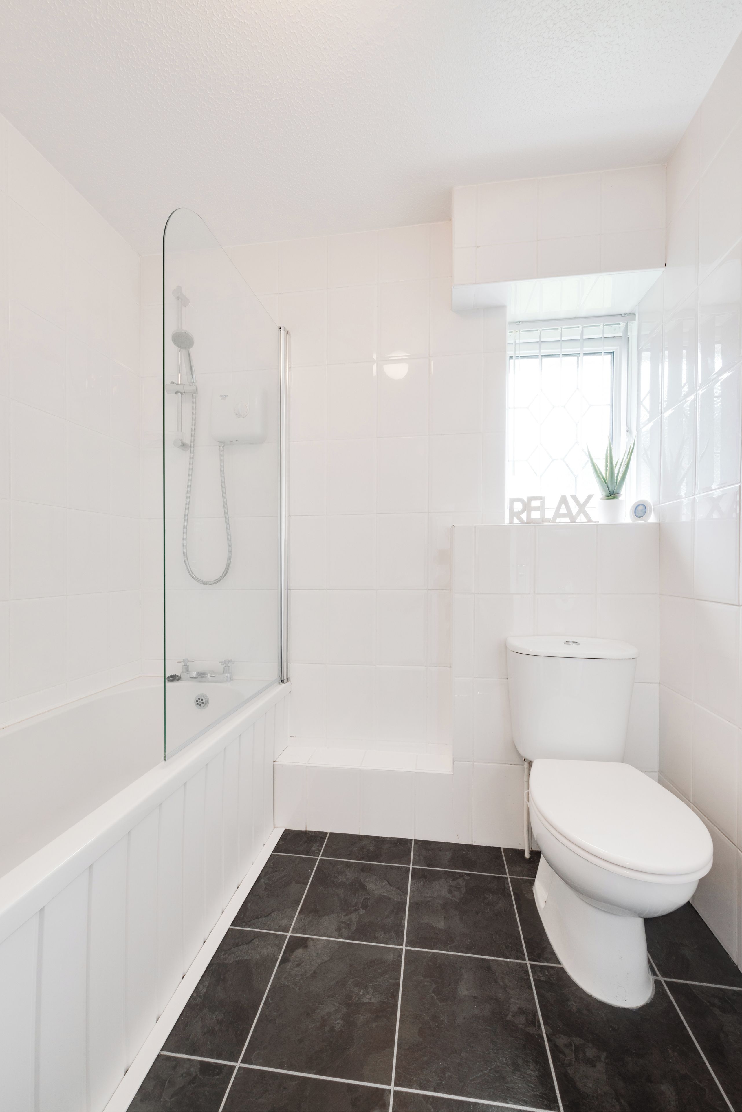Ein Badezimmer mit Dusche, Toilette und einem Fenster mit Pflanze.
