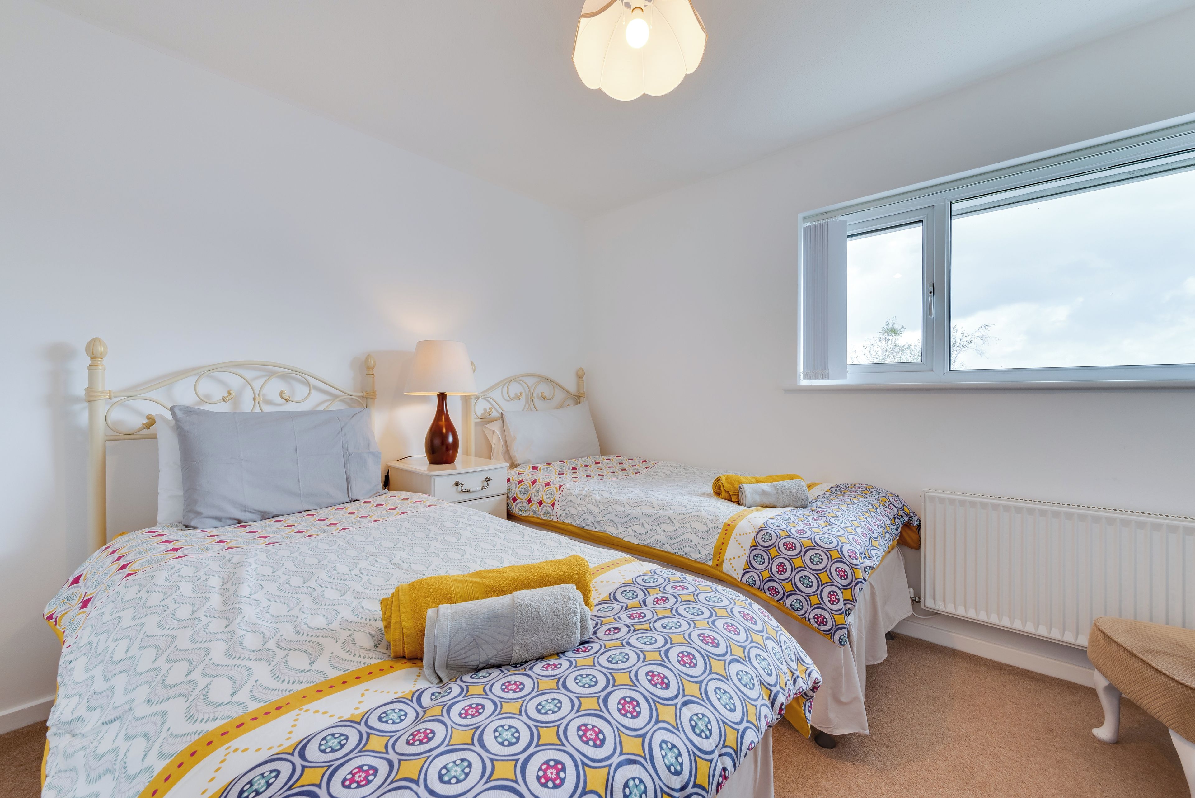 A bedroom with two single beds, a bedside table with a lamp, a window, and a radiator.
