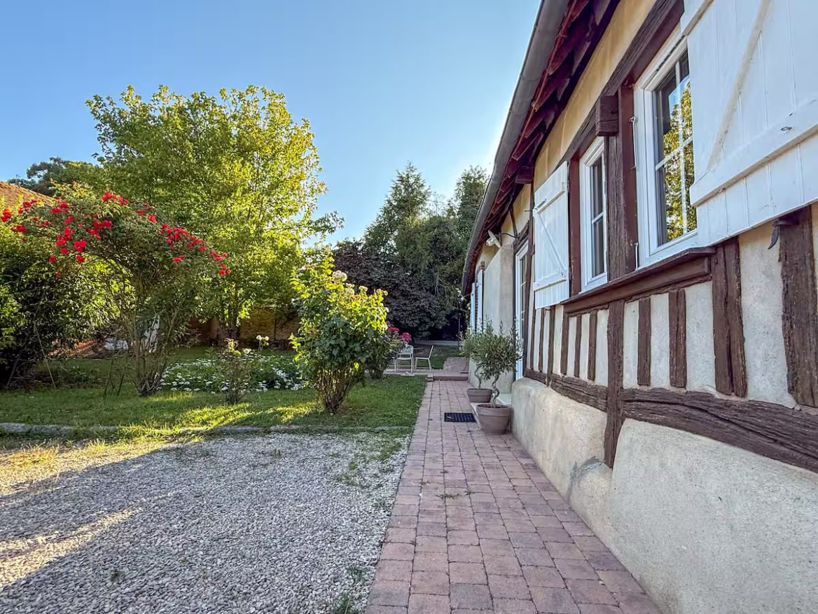 Ein Weg führt zu einem Gebäude mit einer traditionellen Fachwerkausfachung, umgeben von einem Garten mit blühenden Pflanzen und einem Kiesweg.