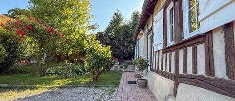 Ein Weg führt zu einem Gebäude mit einer traditionellen Fachwerkausfachung, umgeben von einem Garten mit blühenden Pflanzen und einem Kiesweg.