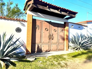 A gated entrance with a metal gate, a brick wall, and agave plants.