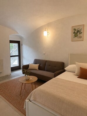 A modern bedroom with a bed, a sofa, a small table with a vase, and a wall-mounted light fixture.
