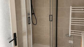A glass-enclosed shower with a handheld showerhead, a white towel rack, and patterned floor tiles.