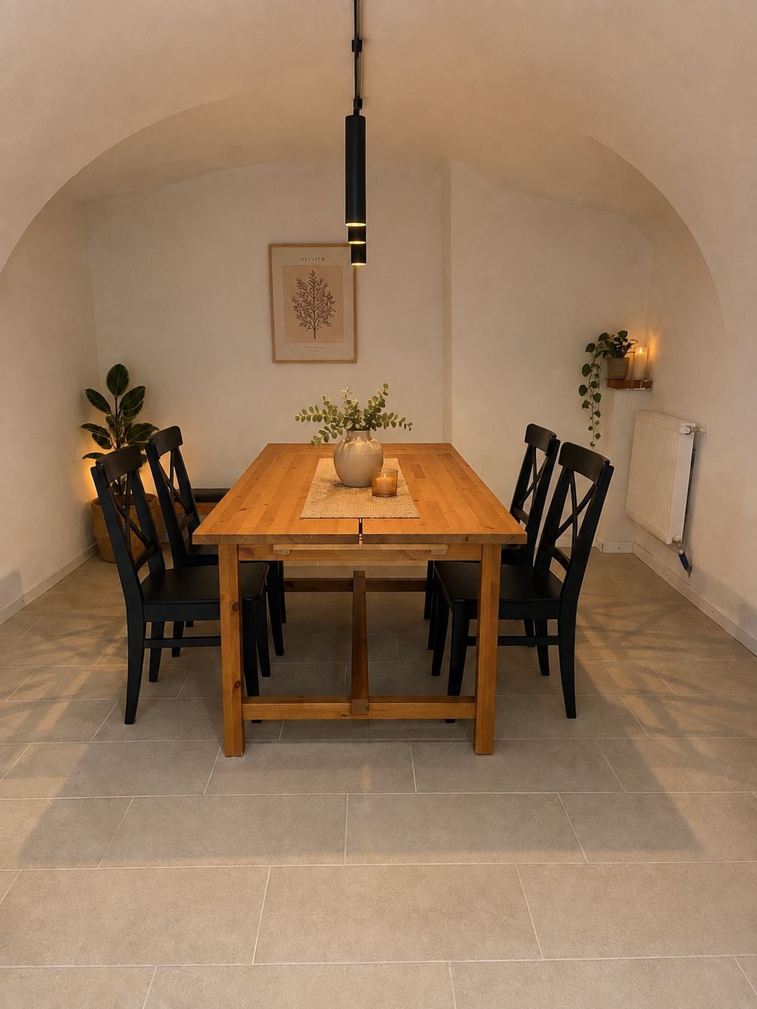 Een eethoek met een houten tafel, zwarte stoelen, een vaas met bloemen, een lijst met een botanische print en een hanglamp.