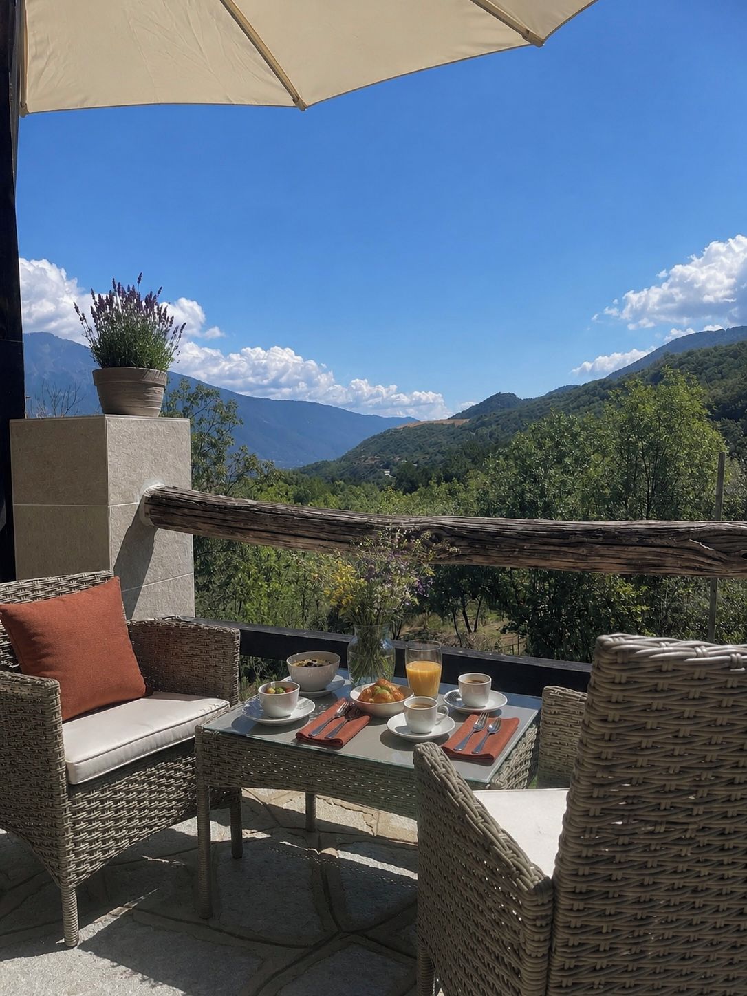 Een terras met rieten meubels, een tafel gedekt met ontbijtartikelen en uitzicht op bergen.