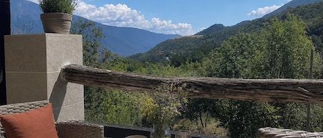 An outdoor seating area with wicker furniture, a table set with breakfast items, and a view of mountains.