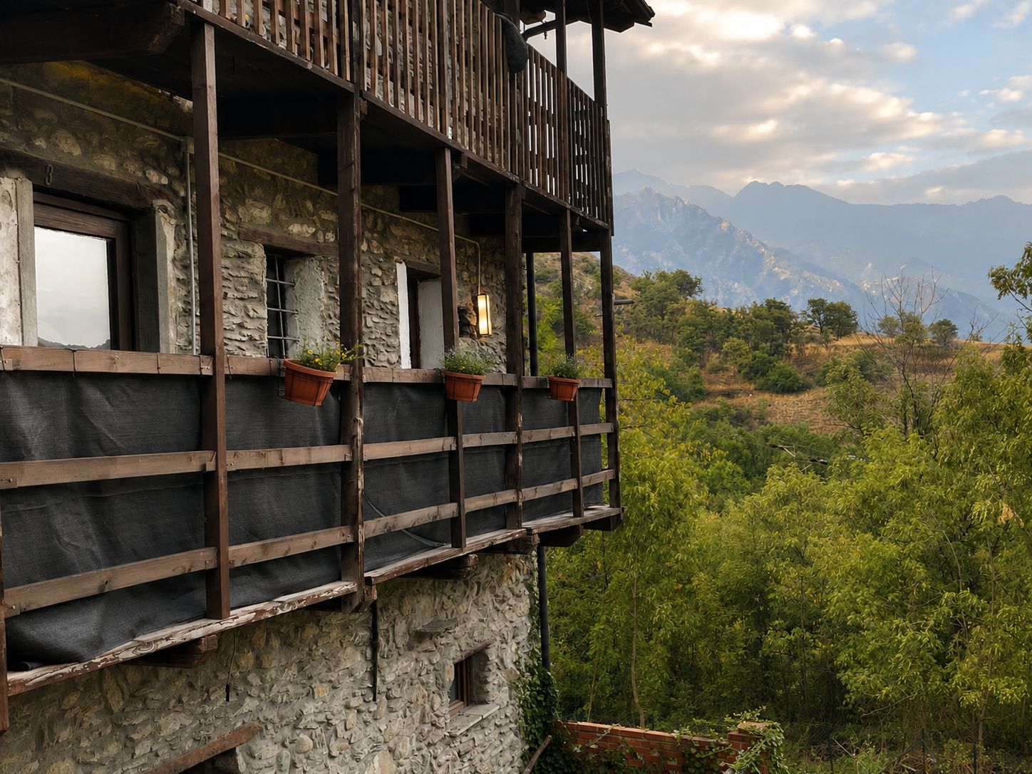 Een gebouw van steen met een houten balkon met uitzicht op een bergachtig landschap.