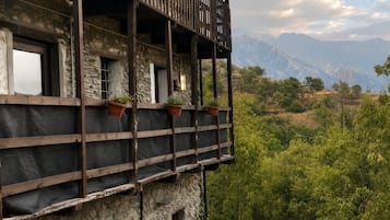 Een gebouw van steen met een houten balkon met uitzicht op een bergachtig landschap.