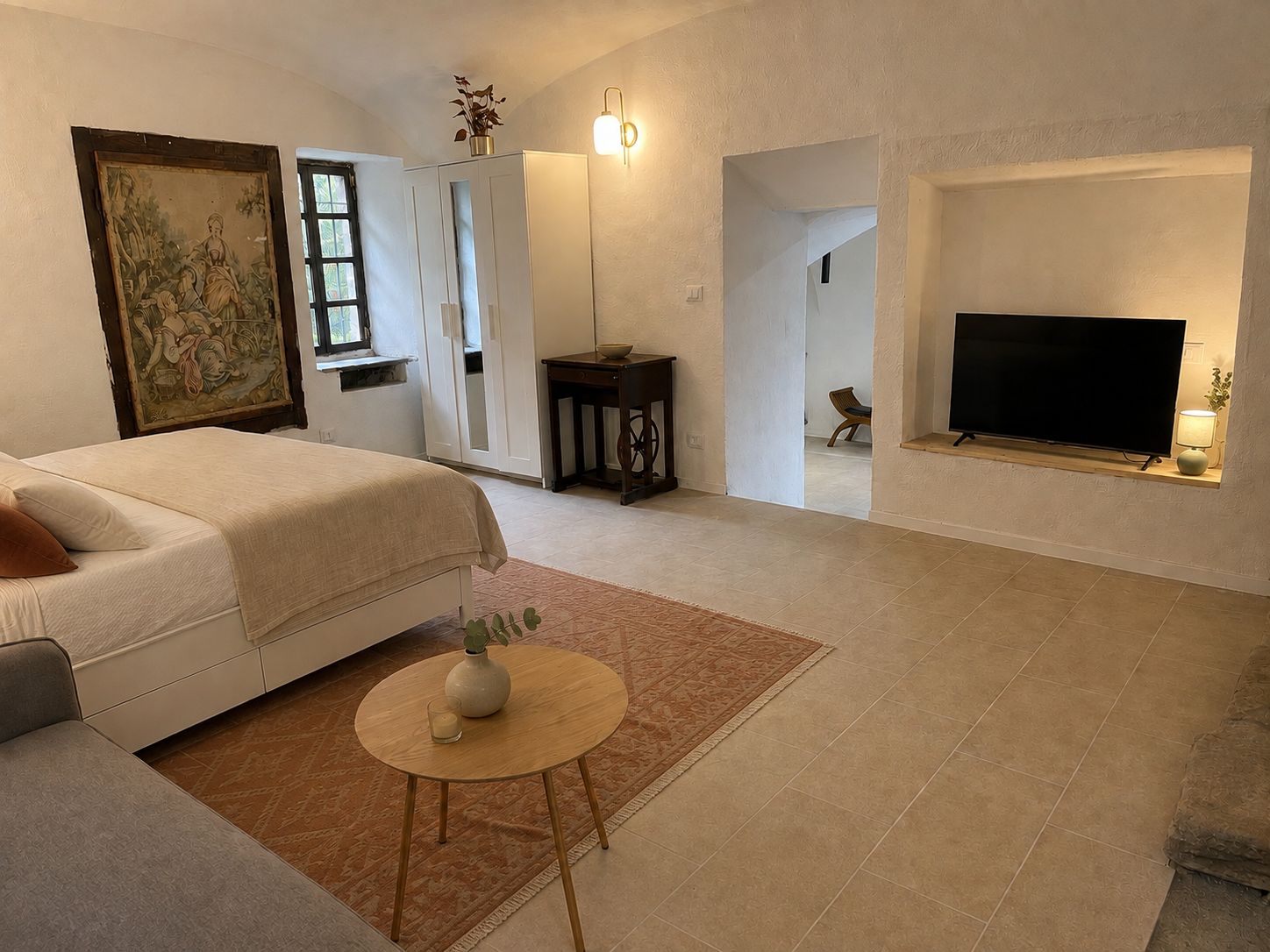 Een moderne slaapkamer met een bed, een klein rond tafeltje met een vaas, een schilderij aan de muur, een televisie en een open haard.