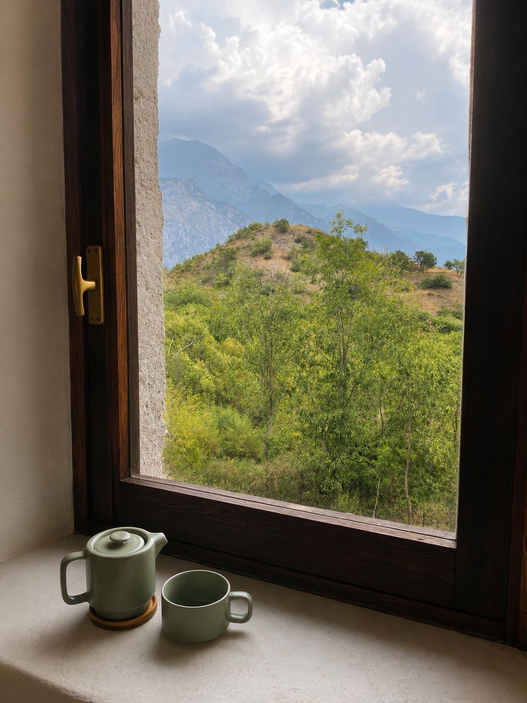 Une fenêtre donnant sur un paysage montagneux, une porte en bois et une petite table avec une théière et une tasse.