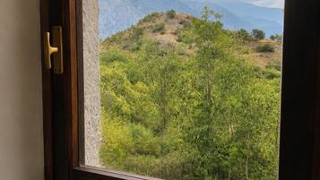 Une fenêtre donnant sur un paysage montagneux, une porte en bois et une petite table avec une théière et une tasse.