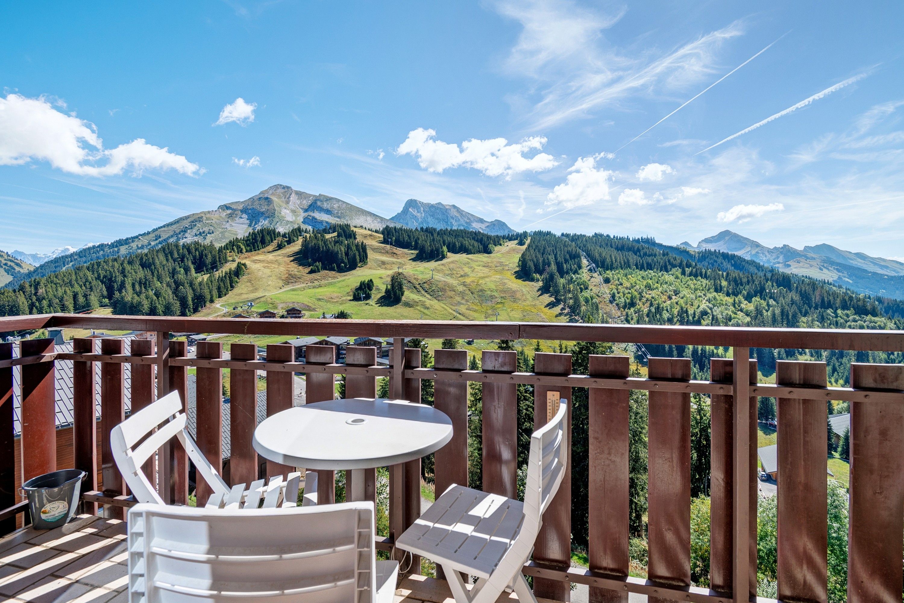 A balcony with a table and chairs, overlooking a mountainous landscape.